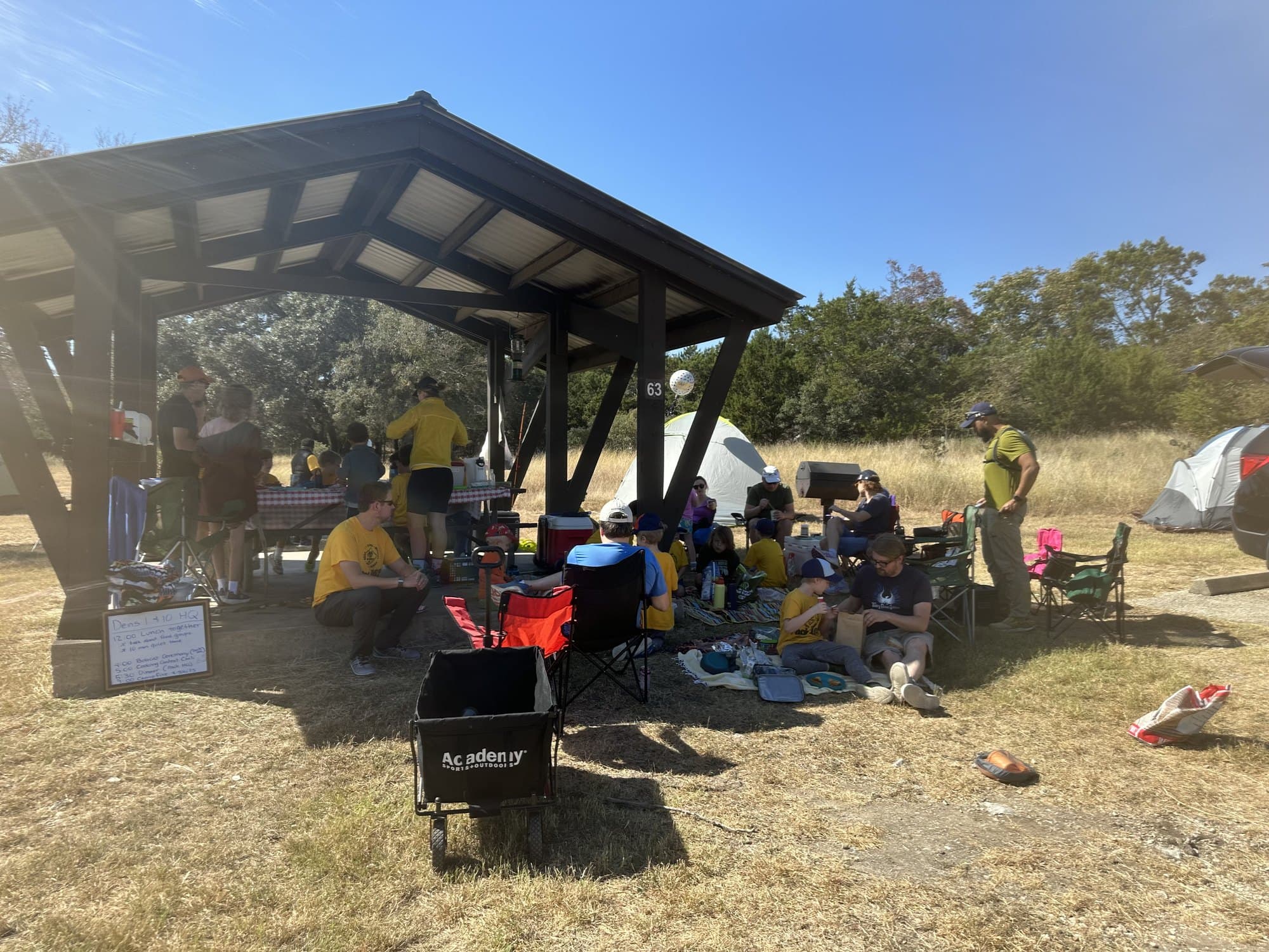 Cub Scout families relaxing under a pavilion at a campground with tents in the background