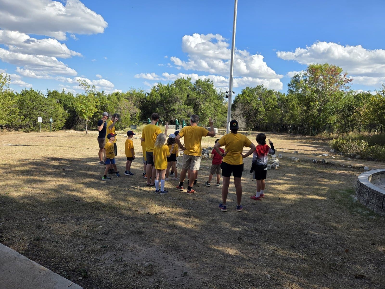 A small group of scouts and adult leaders facing a flagpole outdoors during a flag ceremony