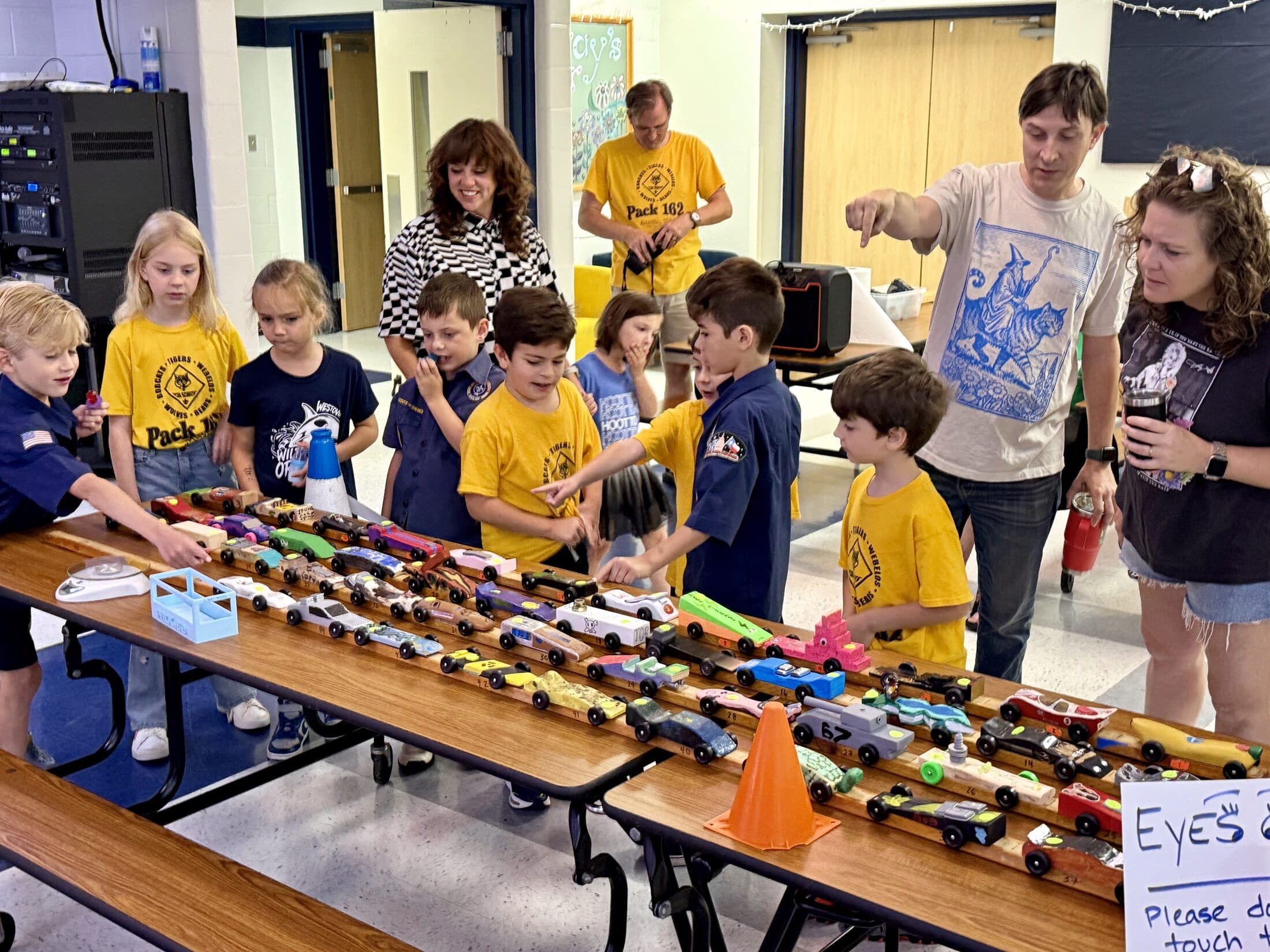Pack 162 scouts and parents gathered around a long table of finished Pinewood Derby cars in the Caraway Elementary cafeteria
