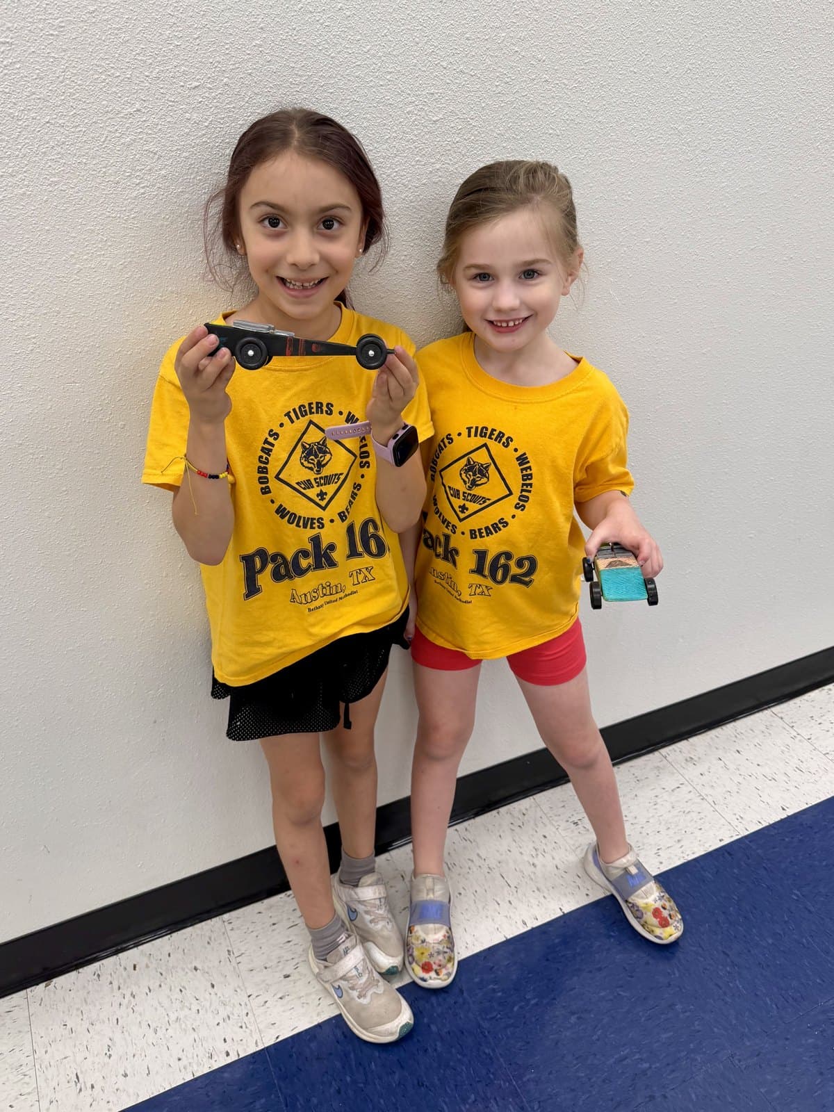 Two young scouts in Pack 162 shirts holding the Pinewood Derby cars they built