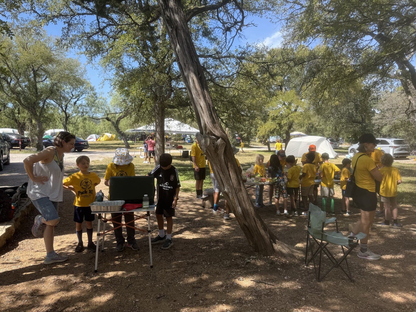 A parent and two Cub Scouts at a camp cooking station with other families gathered nearby