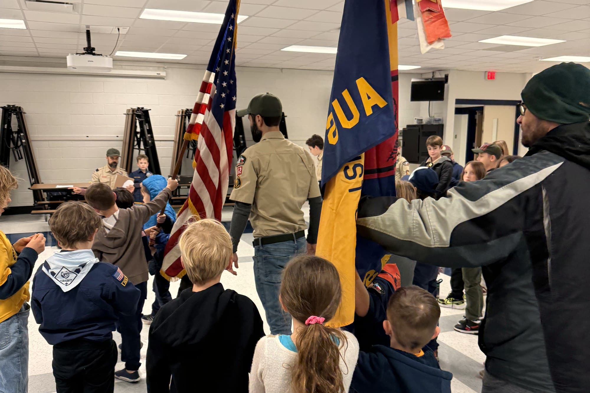 Cub Scouts gathered around a leader carrying the American flag and the Pack 162 flag hung with award ribbons at a pack meeting