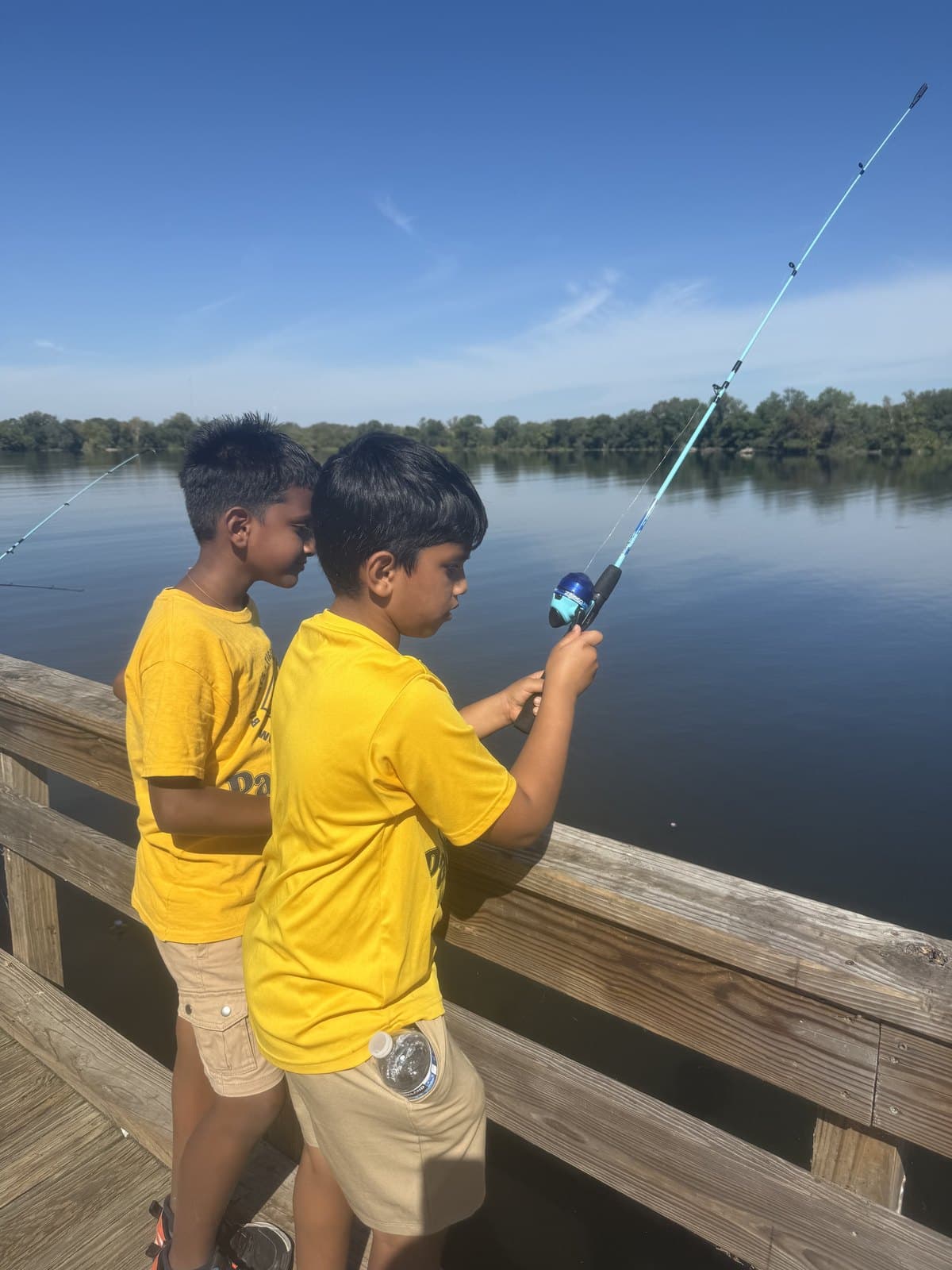 Two Cub Scouts fishing off a wooden dock on a calm lake