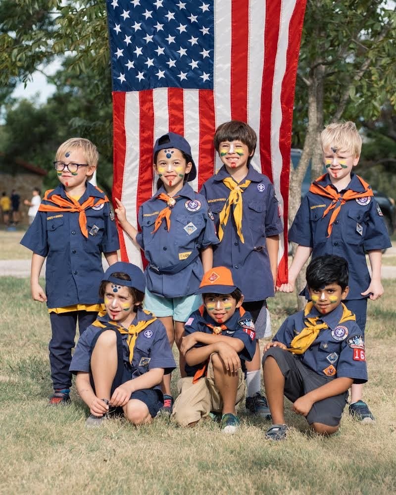 A group of Cub Scouts with painted faces posing together in front of an American flag