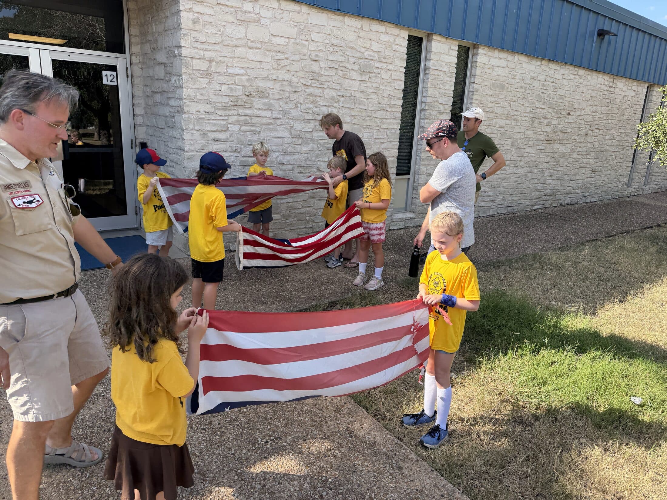 Pack 162 scouts folding the American flag outside Kathy Caraway Elementary with a leader looking on